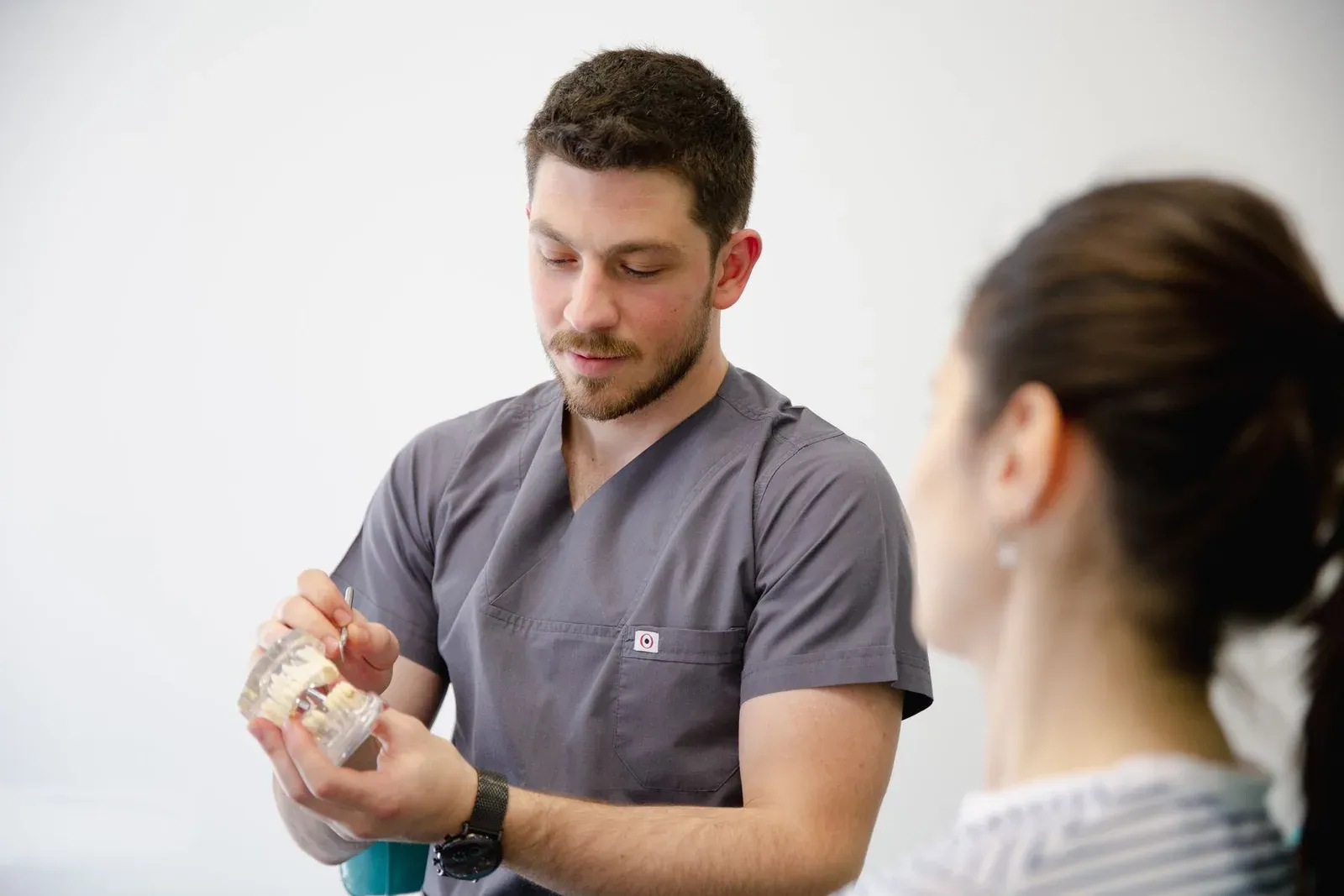 Dentista mostrando um modelo de arcada dentária para uma paciente durante a avaliação.